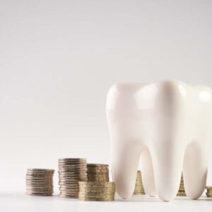 Closeup of a white healthy human tooth model and stacked coins isolated on white background with copy space.